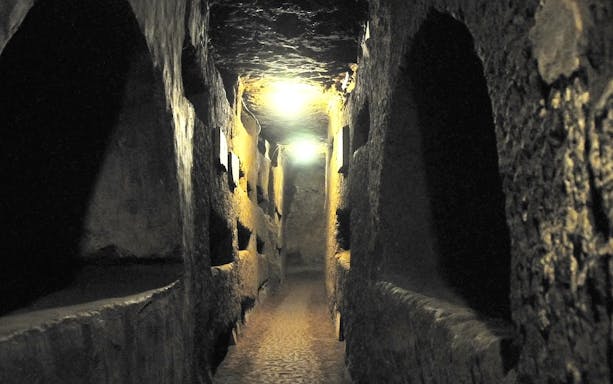 Underground Roman catacombs corridor with illuminated stone walls.