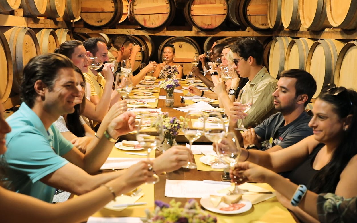 Group enjoying wine tasting in Chianti cellar with wooden barrels.
