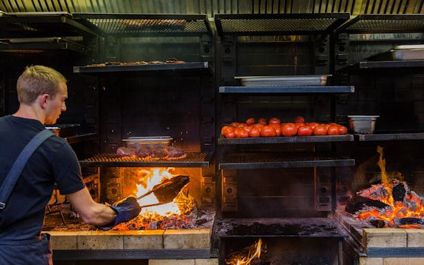 Chef grilling meat and tomatoes over open flame at City Winery Wine and Food Pairing Experience.