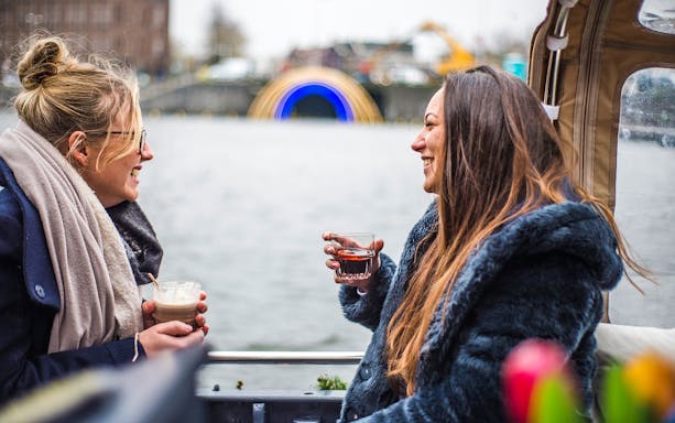 Two people enjoying drinks on an Amsterdam Light Festival canal cruise.