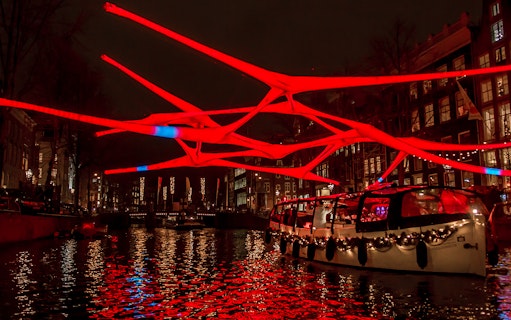 Amsterdam canal cruise with illuminated red art installation during Light Festival.