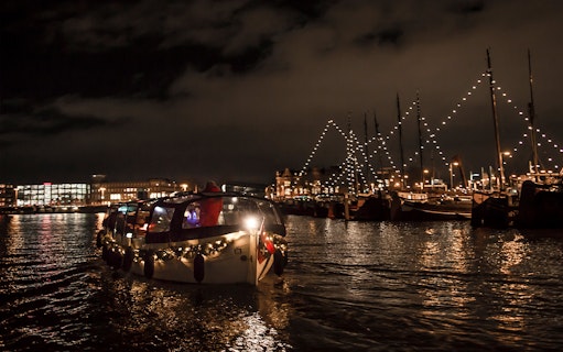Amsterdam canal cruise at night with festive lights and onboard bar.