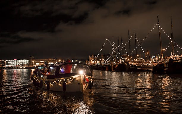 Amsterdam canal cruise at night with festive lights and onboard bar.
