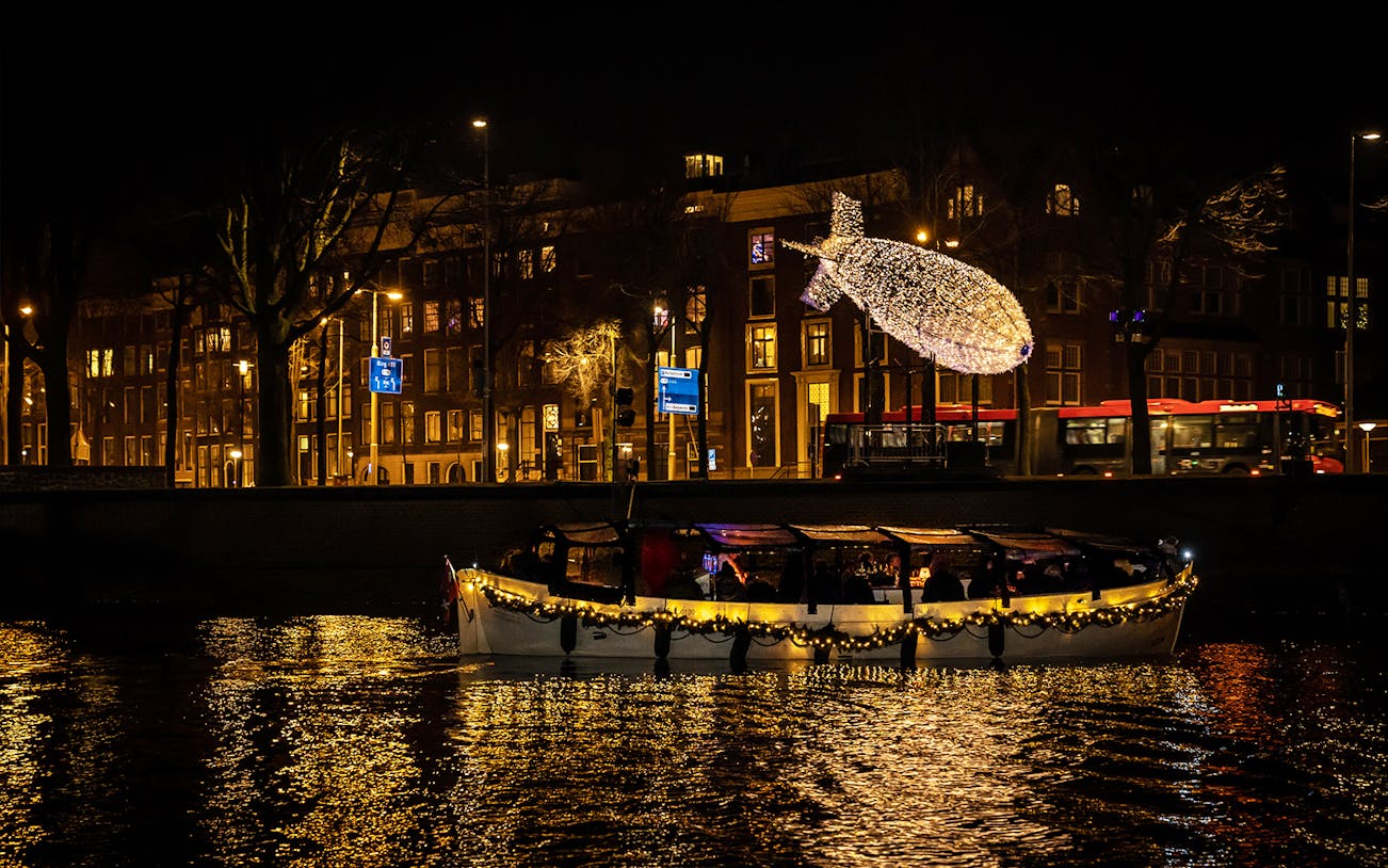Amsterdam canal cruise with illuminated fish sculpture during Light Festival.