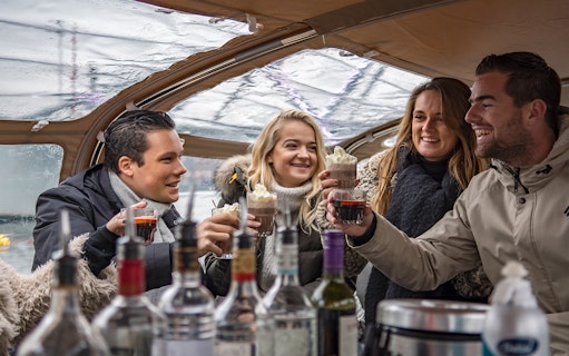 Group enjoying drinks on Amsterdam Light Festival canal cruise with onboard bar.