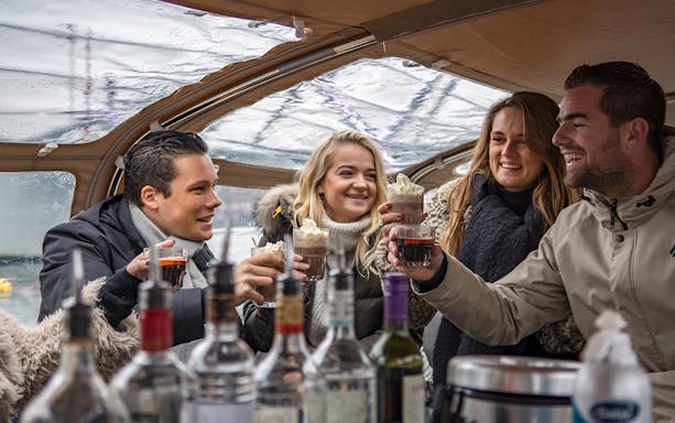 Group enjoying drinks on Amsterdam Light Festival canal cruise with onboard bar.