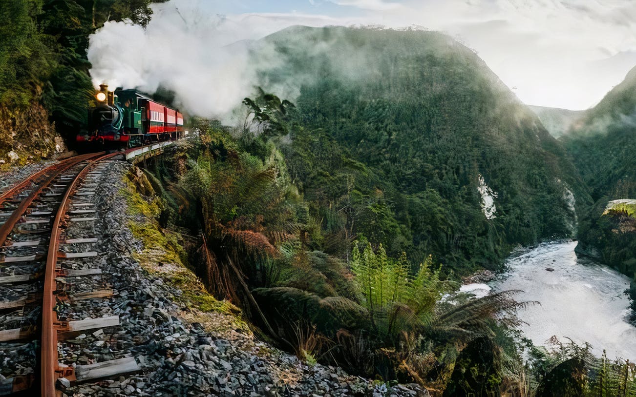 Steam train traveling through King River Gorge with lush greenery and river below.