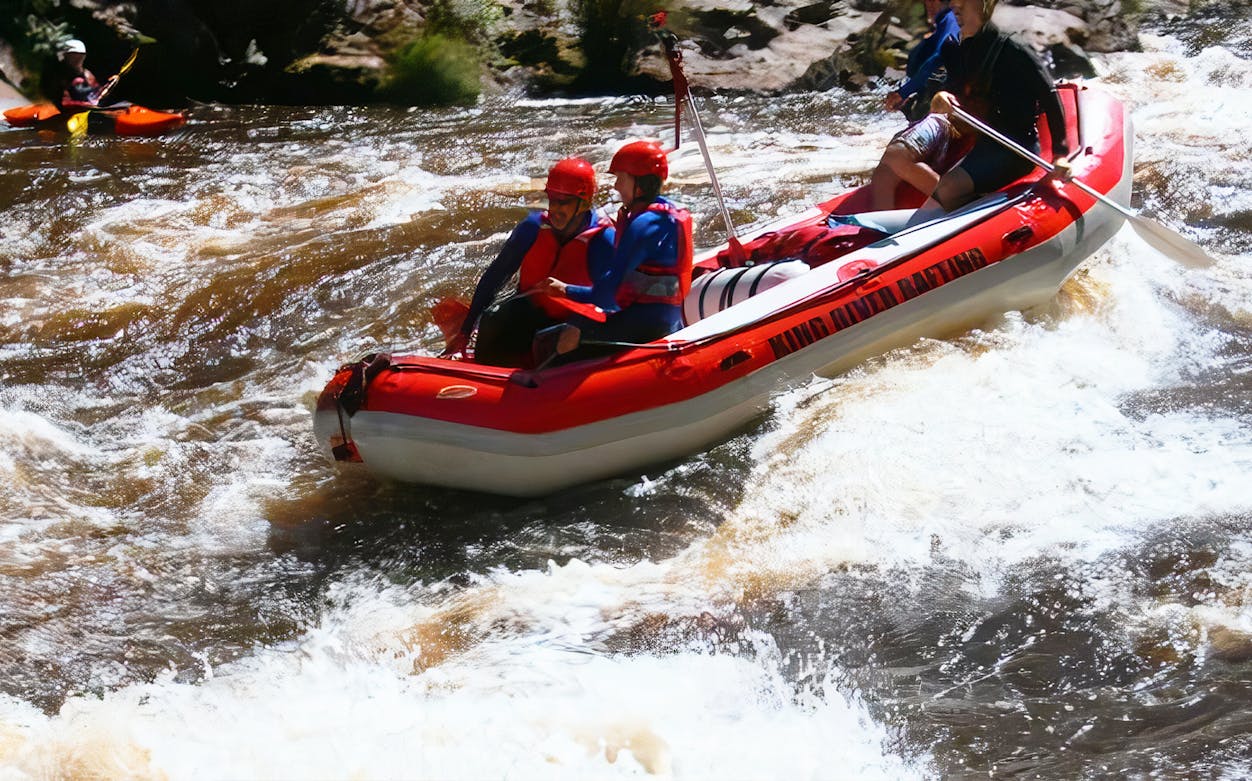 Whitewater rafting adventure on a river with participants in a red raft, wearing helmets and life jackets.