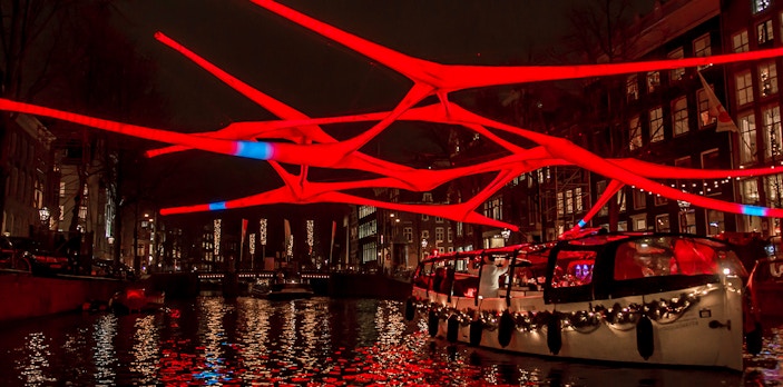 Luxury canal cruise under illuminated red art installation at Amsterdam Light Festival.