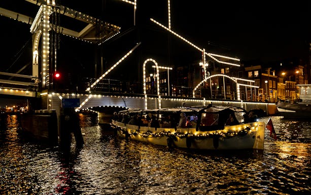 Luxury canal cruise passing illuminated bridge during Amsterdam Light Festival.