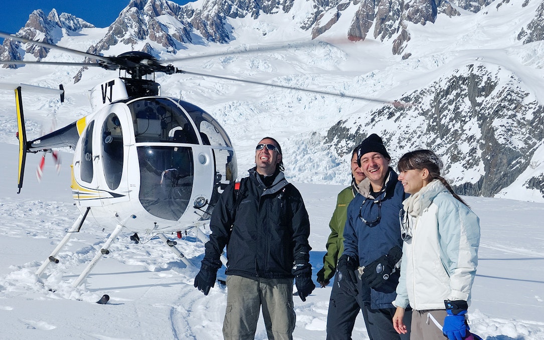 Helicopter tour group on snow at Fox Glacier with Mount Cook in background.