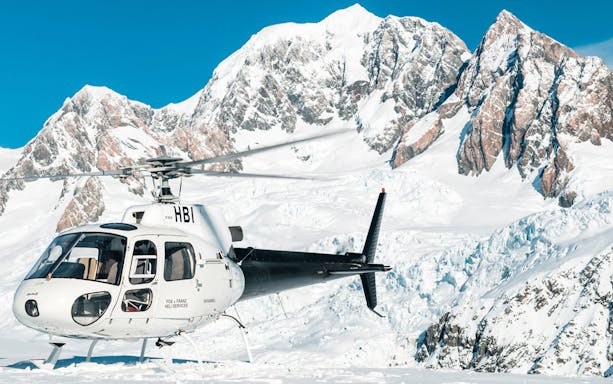 Helicopter on snow with Fox Glacier and Mount Cook in background.