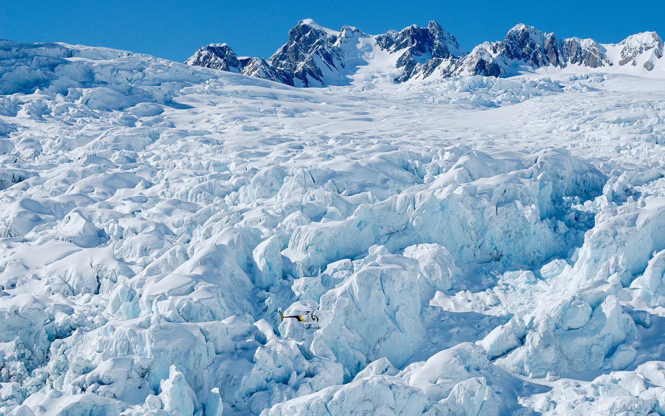 Helicopter flying over Fox Glacier with Mount Cook in the background.