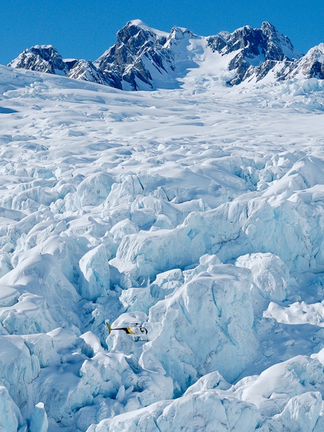 Helicopter flying over Fox Glacier with Southern Alps in the background.