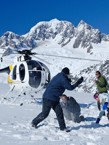 Helicopter landing on snowy mountain with people playing in snow, Fox & Franz Scenic Flight.
