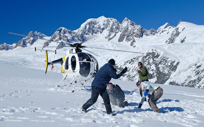 Helicopter landing on snowy mountain with people playing in snow, Fox & Franz Scenic Flight.