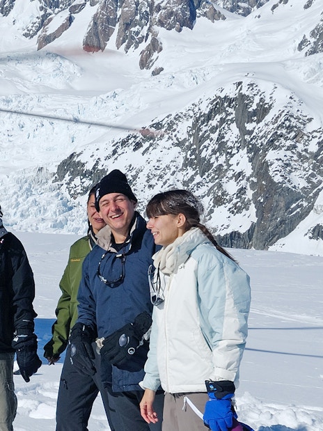 Helicopter tour group on snowy Fox Glacier with mountain backdrop.