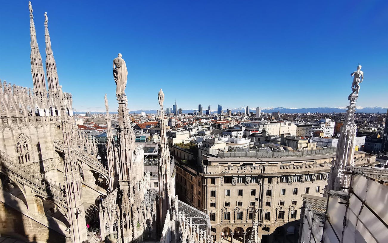 Milan Duomo rooftop view with city skyline and cathedral spires.