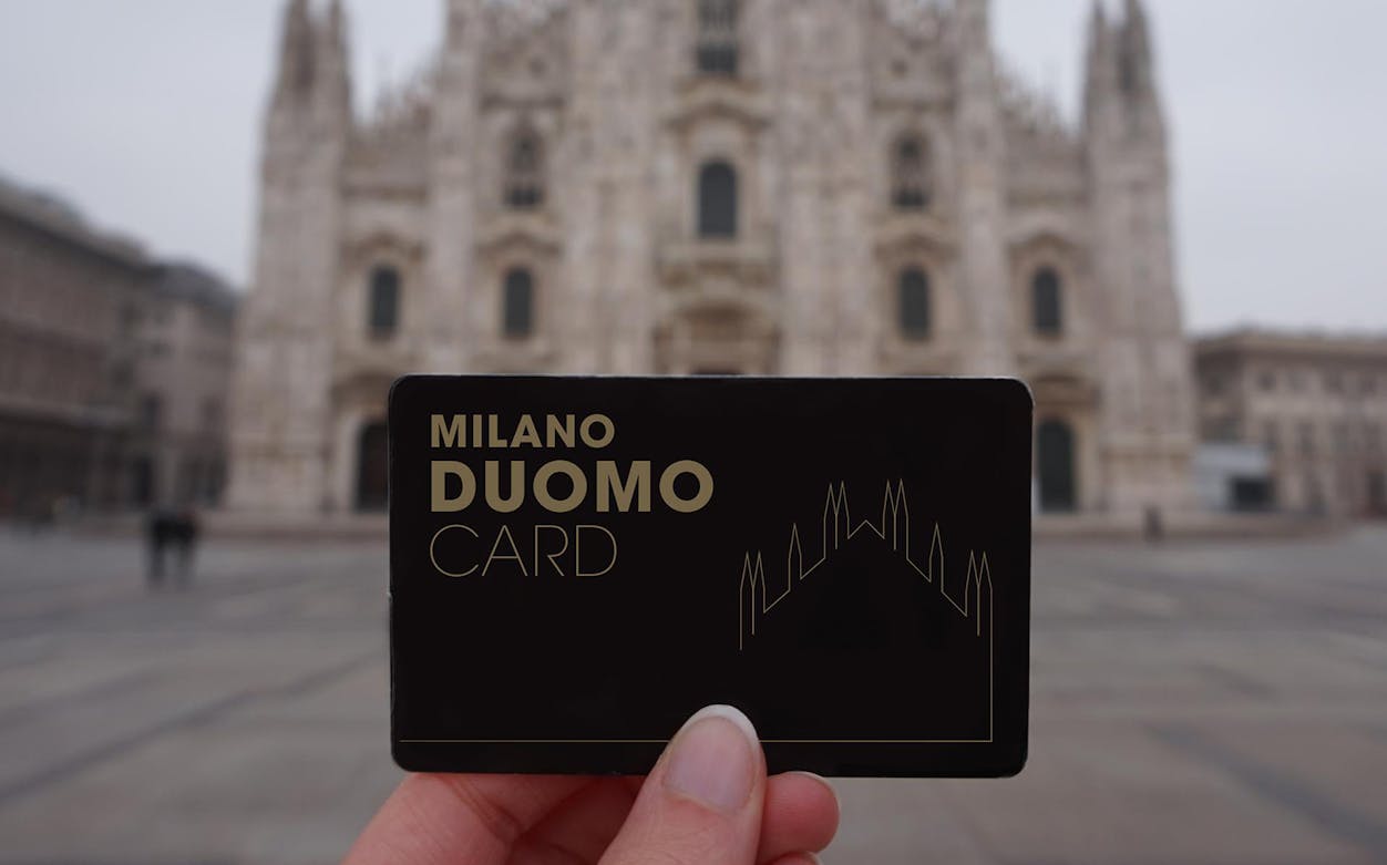 Milan Duomo Pass held in front of the cathedral facade.