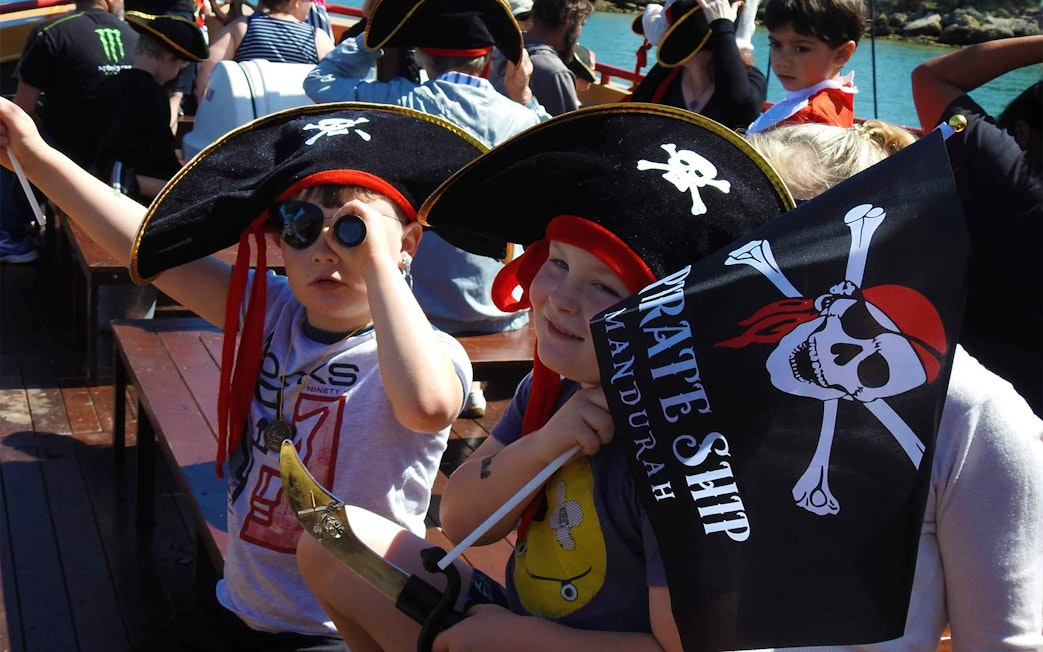 Children dressed as pirates on the Pirate Ship Mandurah holding a flag and telescope.