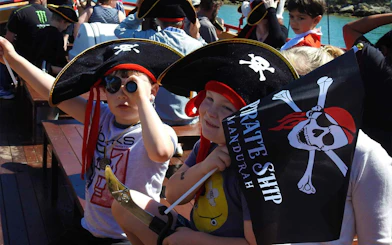 Children dressed as pirates on the Pirate Ship Mandurah holding a flag and telescope.