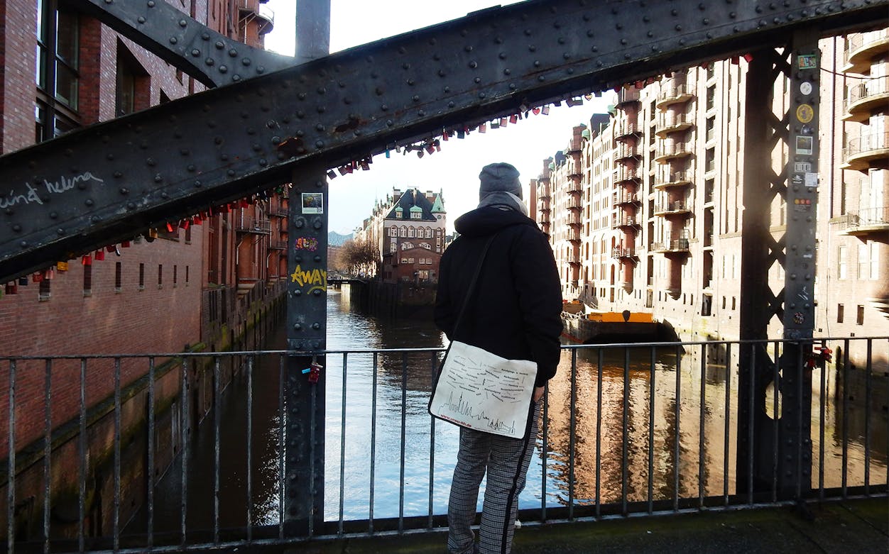 Person standing on a bridge in Hamburg's Speicherstadt district, surrounded by historic brick warehouses.
