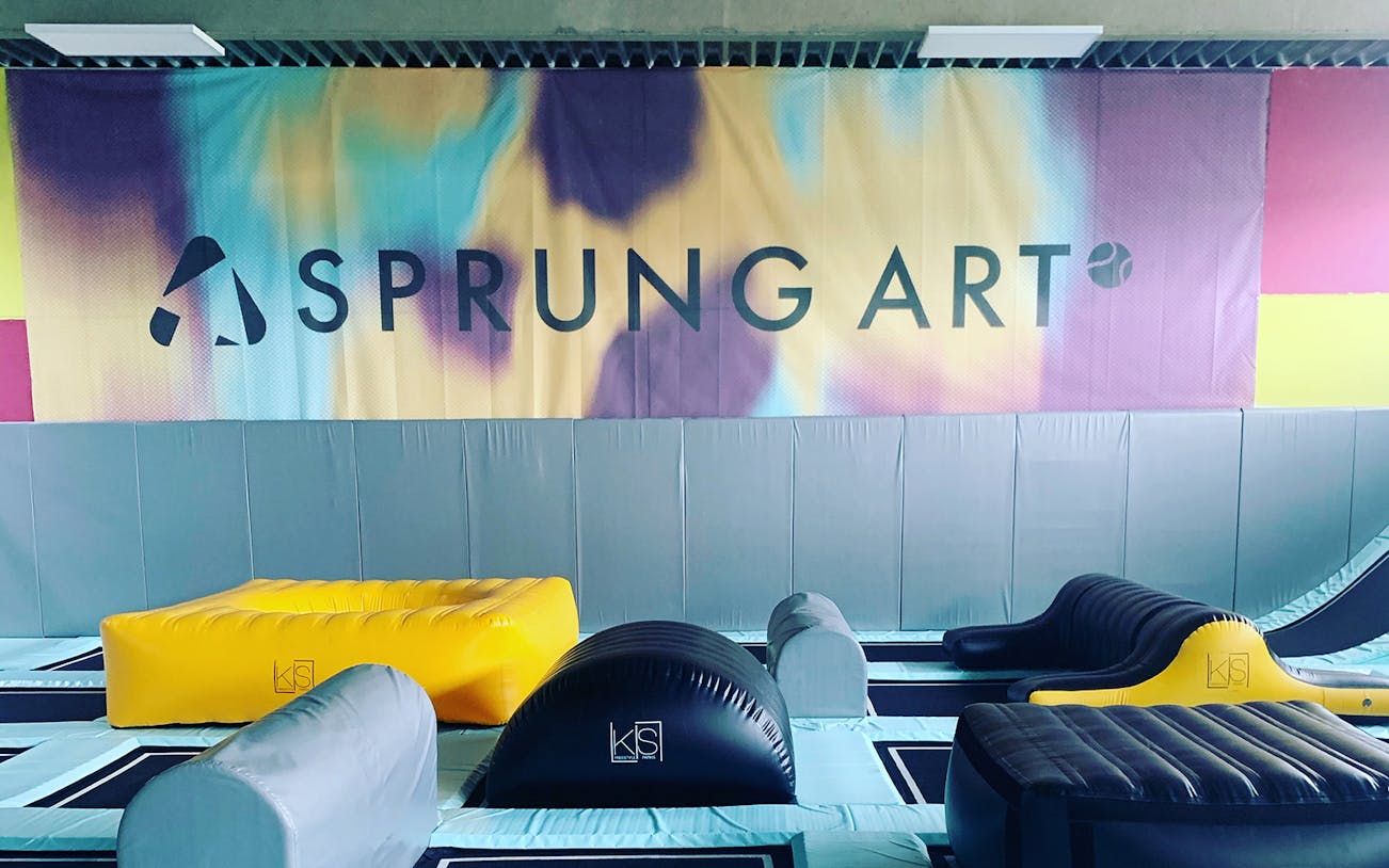 Indoor trampoline park with colorful padded obstacles and "Sprung Art" sign.