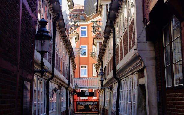 Narrow alleyway in Hamburg with historic brick buildings and Krameramtsstuben sign.