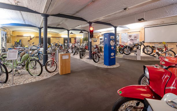 Motorcycle display at DDR Museum, featuring vintage bikes and a blue gas pump.