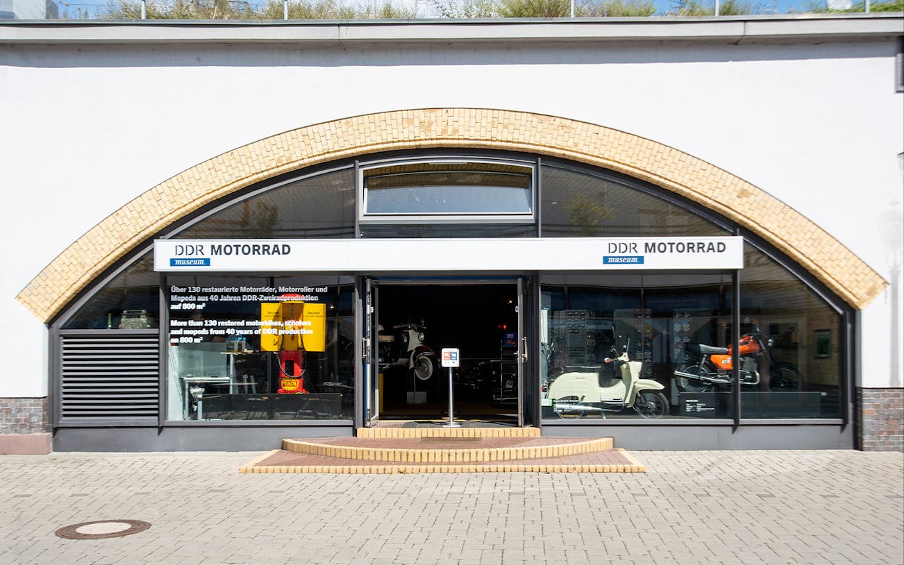 Entrance to DDR Museum motorcycle exhibition in Berlin displaying vintage scooters and motorbikes.