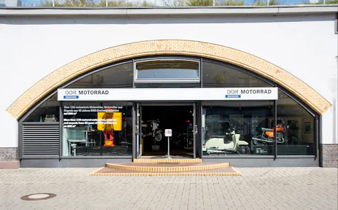 Entrance to DDR Museum motorcycle exhibition in Berlin displaying vintage scooters and motorbikes.