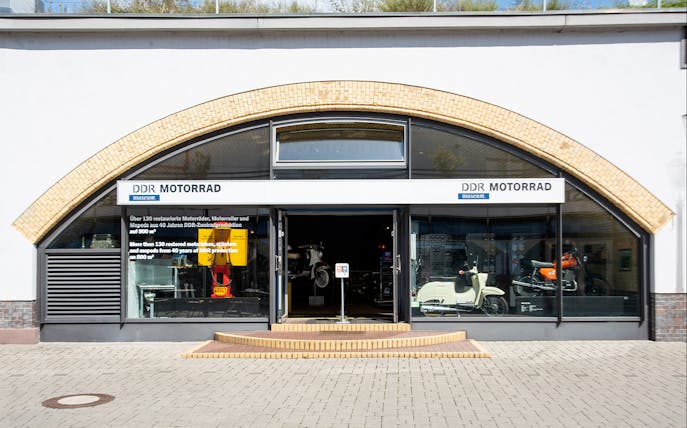 Entrance to DDR Museum motorcycle exhibition in Berlin displaying vintage scooters and motorbikes.