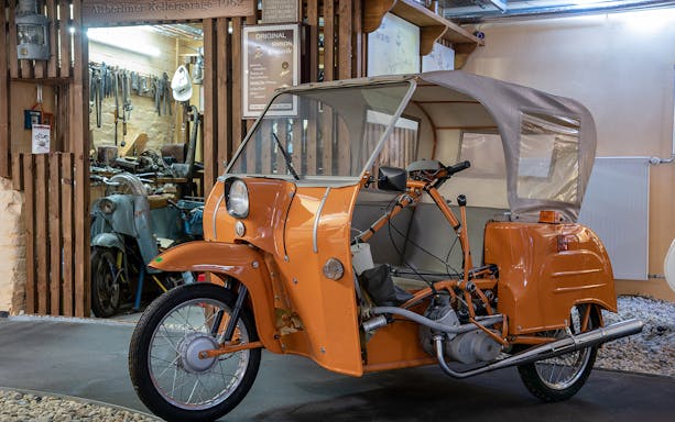 Vintage orange motorcycle at DDR Museum entrance, Berlin.