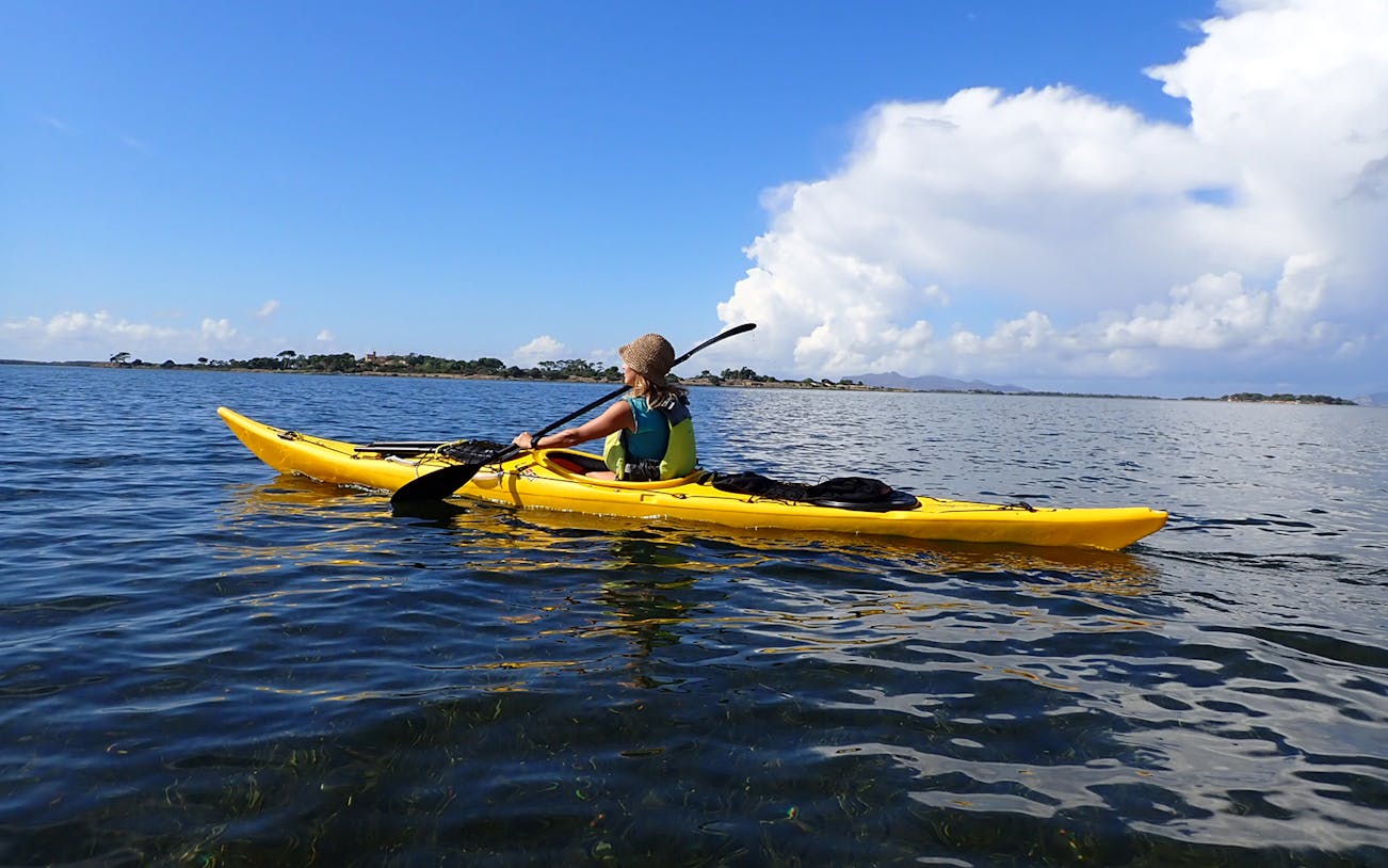 Kayaker paddling in Stagnone Nature Reserve, Sicily, with distant shoreline.