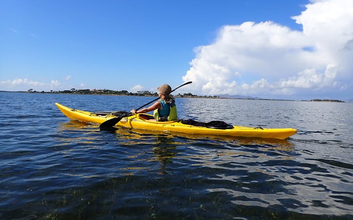 Kayaker paddling in Stagnone Nature Reserve, Sicily, with distant shoreline.