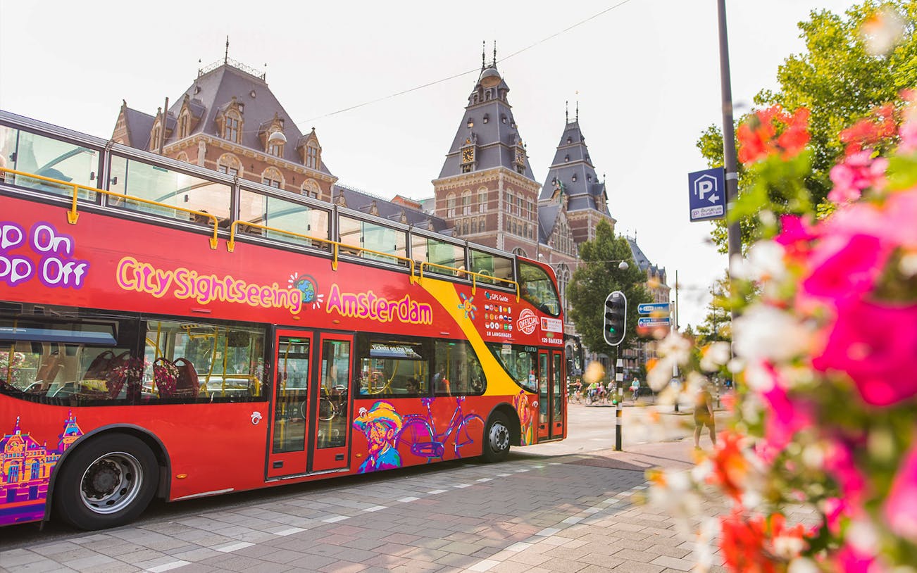 Red double-decker bus for Amsterdam hop-on hop-off tour near historic building.