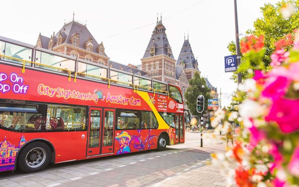 Red double-decker bus in front of the Rijksmuseum, Amsterdam, for hop-on hop-off tour.
