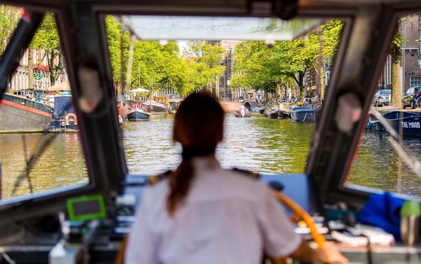 Boat navigating Amsterdam canal during half-day hop-on hop-off tour.