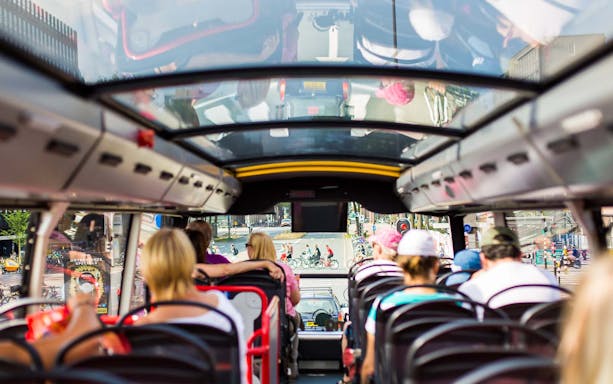 Interior view of a tour bus with passengers, city street visible through the front window.