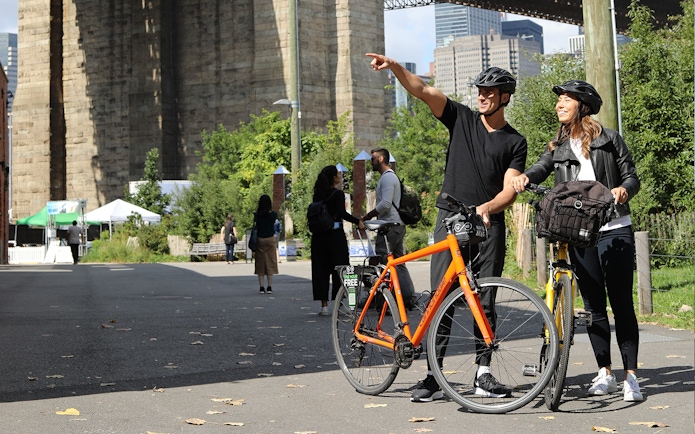 Couple with bikes near Brooklyn Bridge, New York City, enjoying a guided tour.