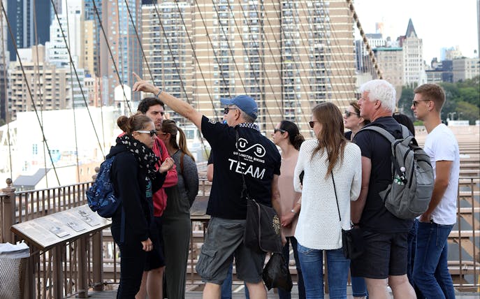 Tour group on Brooklyn Bridge with guide explaining city landmarks.