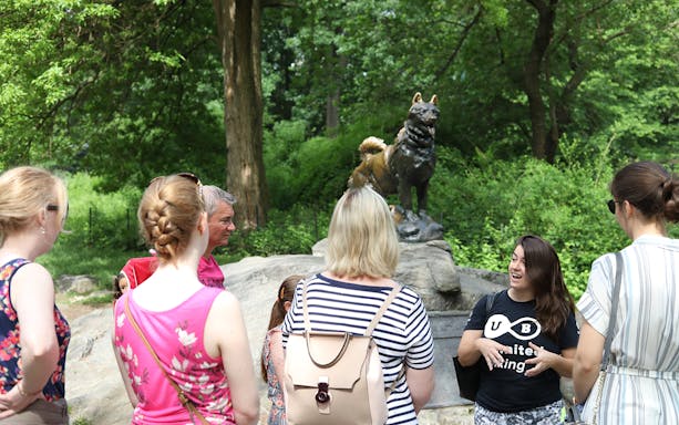 Group of tourists listening to a guide near the Balto statue in Central Park.