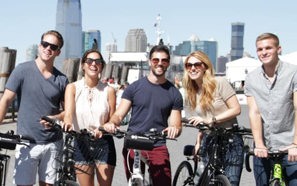 Group of people on bikes with New York City skyline in the background.