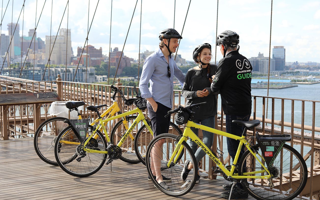 Cyclists with a guide on Brooklyn Bridge during a bike tour, New York City skyline in background.