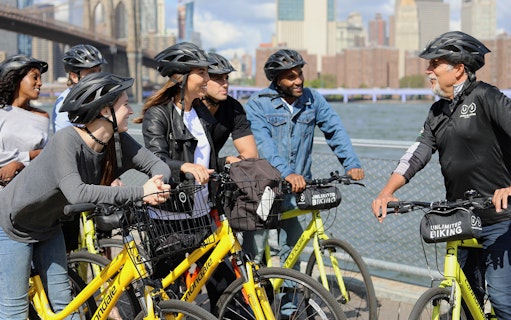 Group of cyclists on Brooklyn Bridge bike tour with city skyline in background.