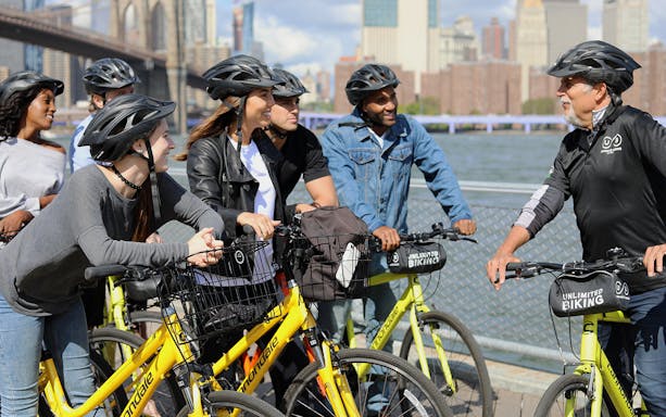 Group of cyclists on Brooklyn Bridge bike tour with city skyline in background.