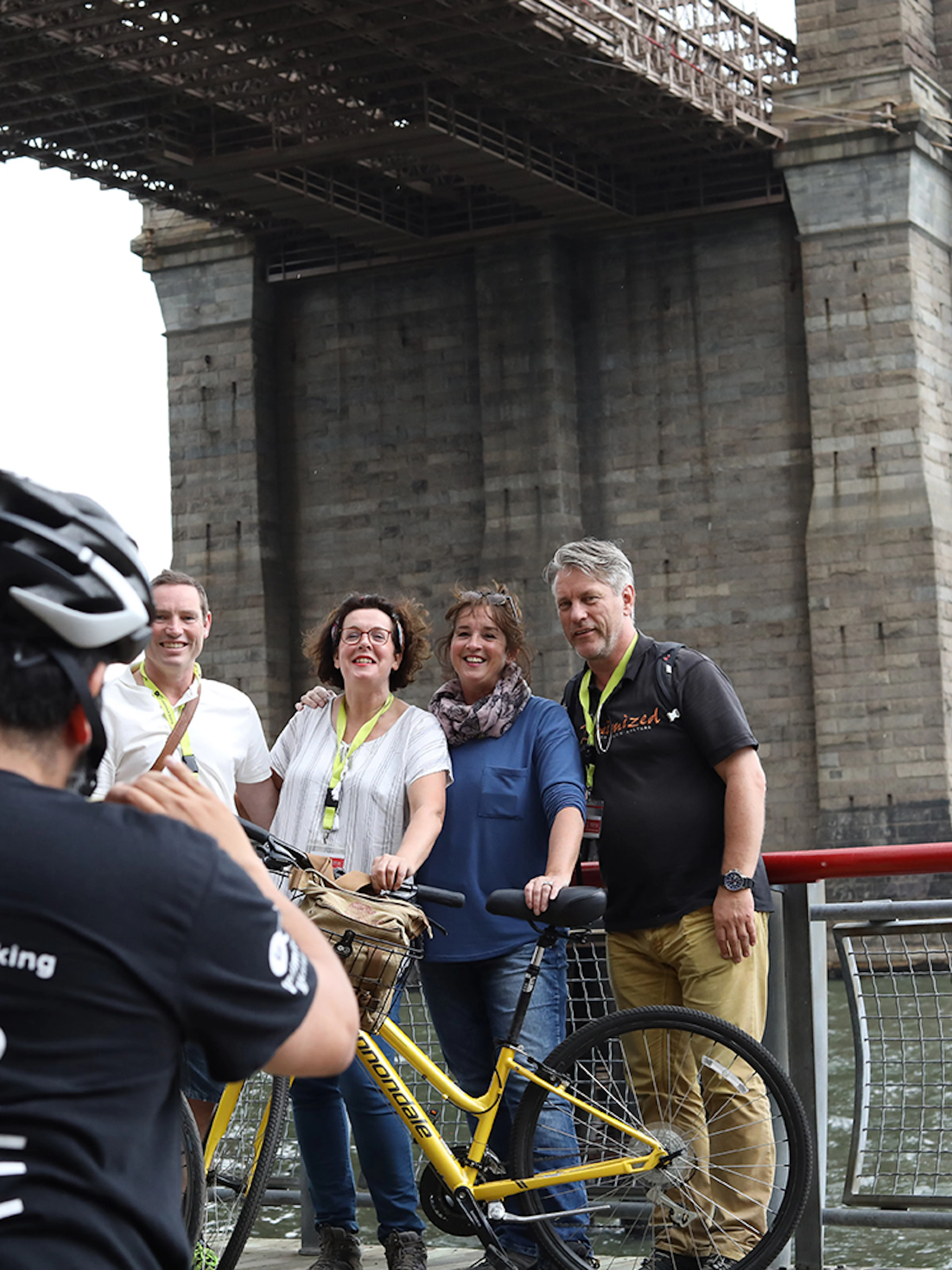 Group posing with bikes under Brooklyn Bridge during tour.