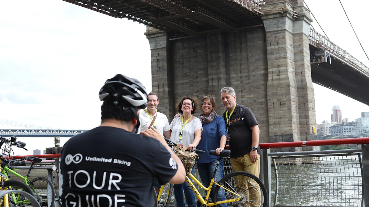 Group posing with bikes under Brooklyn Bridge during tour.