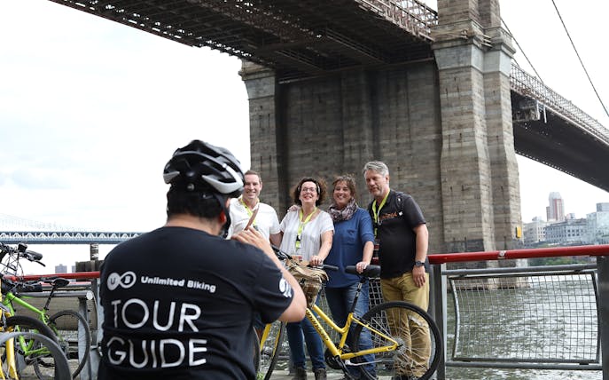 Group posing with bikes under Brooklyn Bridge during tour.