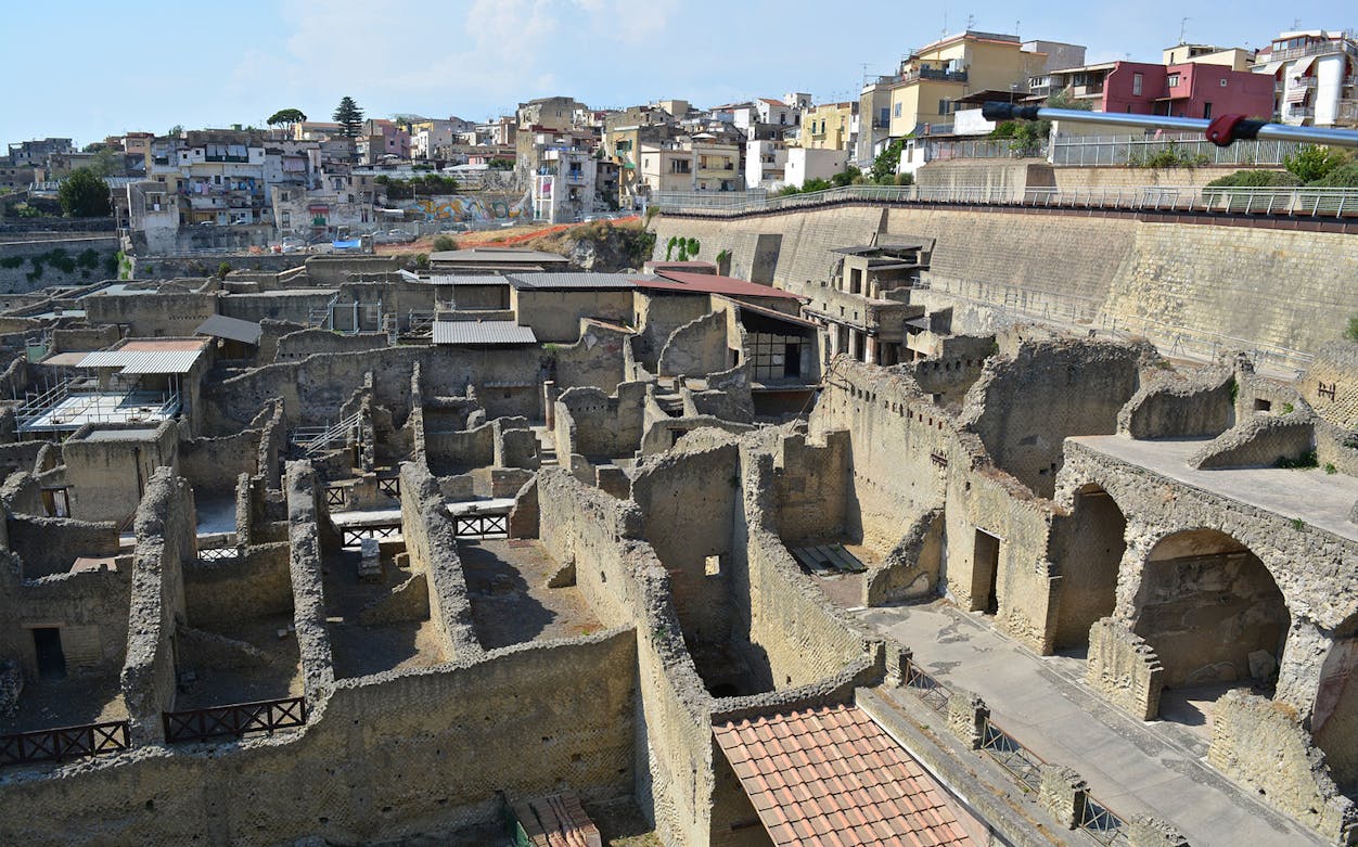 Herculaneum Archaeological Park ruins with surrounding modern buildings in the background.